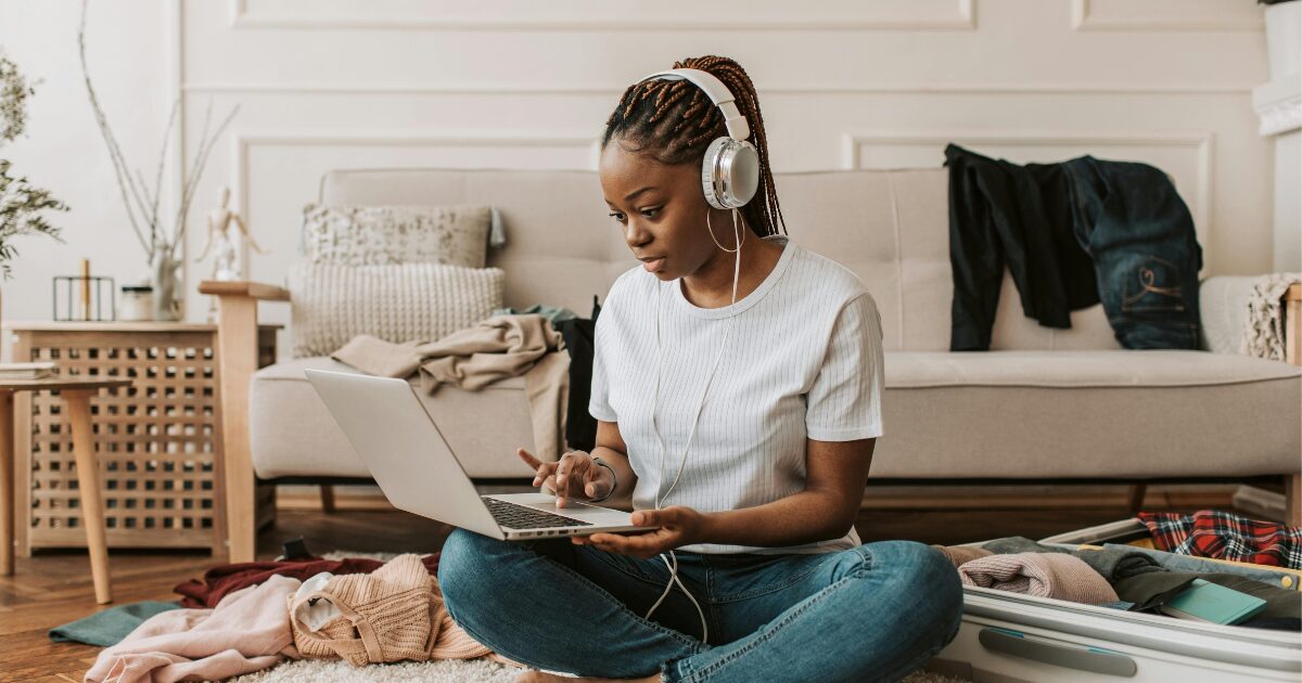 321 A Black woman wearing a white shirt sitting on the floor with a laptop on her lap
