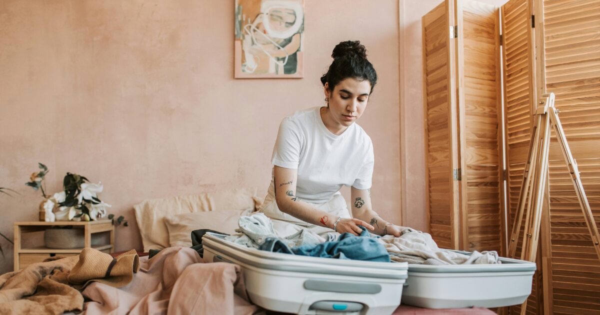 334 A Caucasian woman wearing a white shirt packing her clothes on a white luggage.