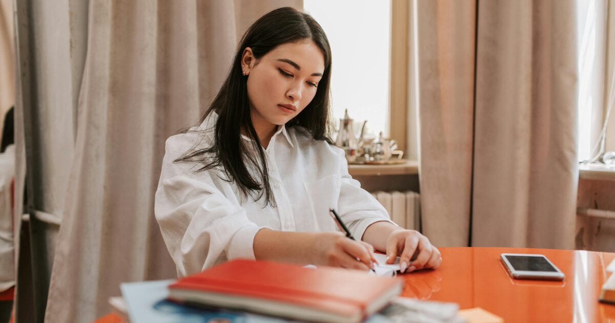 336 An East Asian woman wearing a white blouse writing on a document.