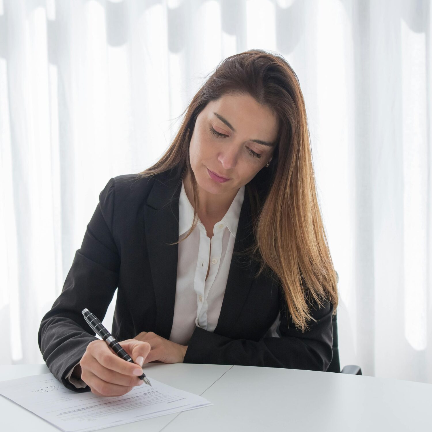 A Caucasian woman wearing a black blazer writing on a piece of paper.
