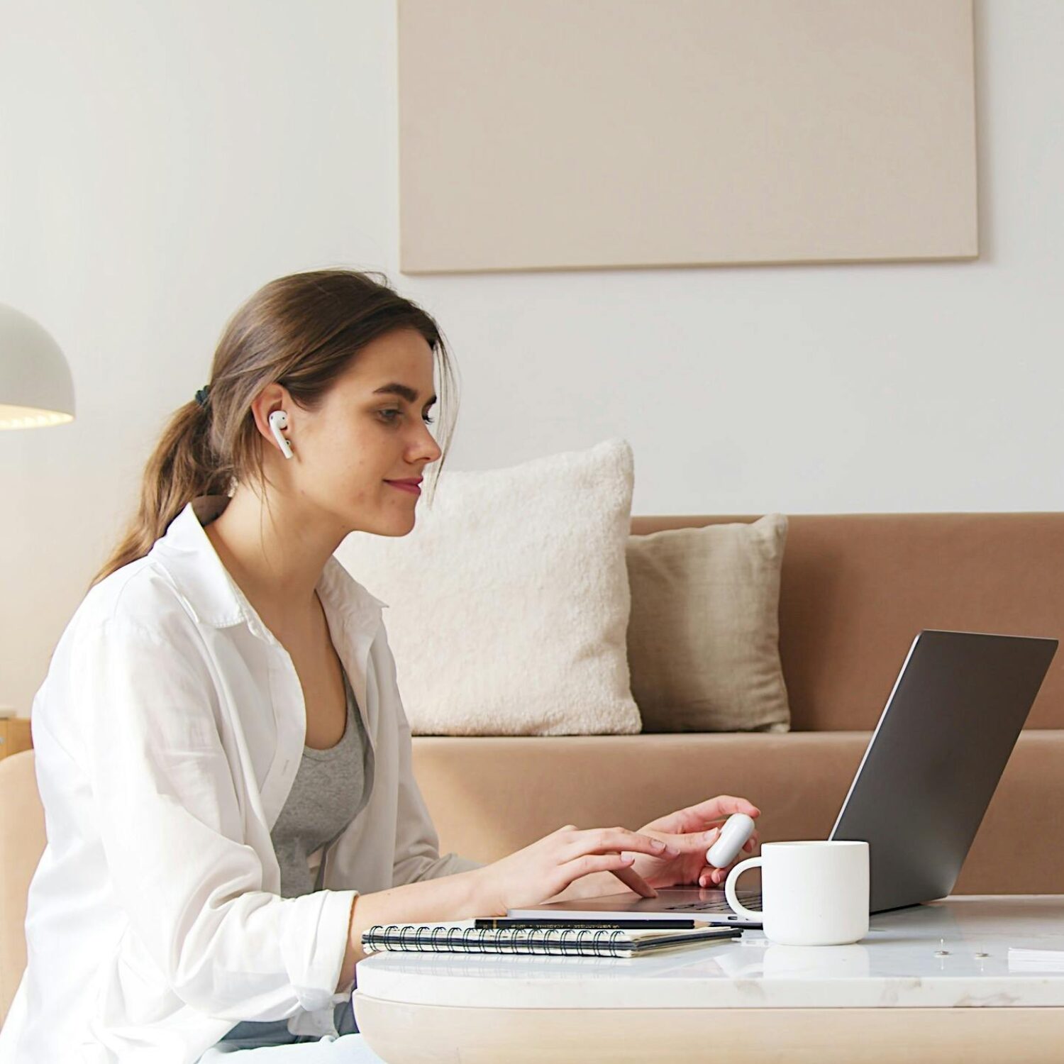 A Caucasian woman wearing a white blouse smiling while sitting in front of a laptop