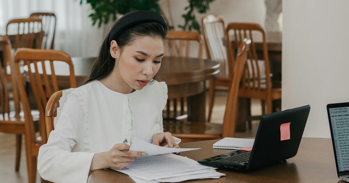In-Blog Thumbnails (2) A Caucasian woman wearing a white dress reading a document while sitting in front of an open laptop.