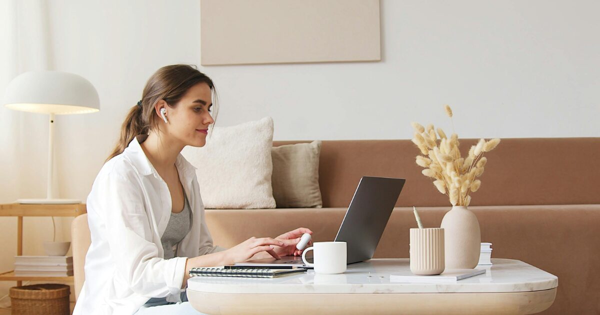 A Caucasian woman wearing a white blouse smiling while sitting in front of a laptop 