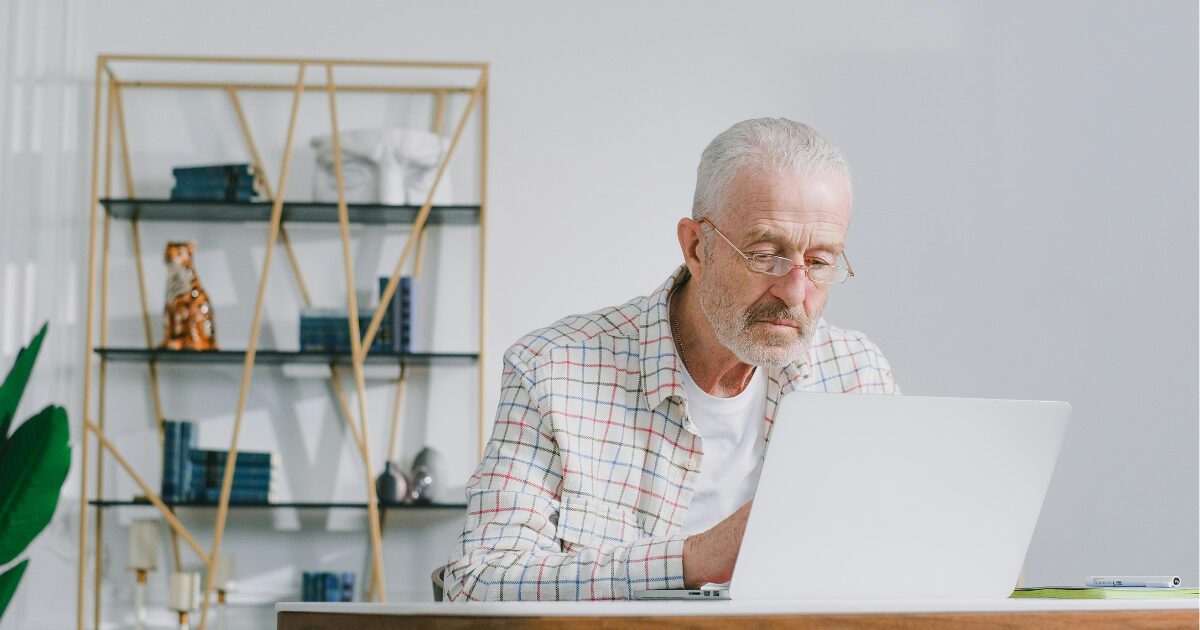 An Elderly Caucasian man wearing a white checkered shirt using a laptop