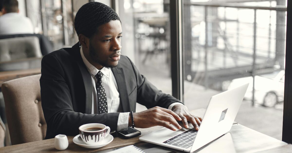 A Black man wearing a black business suit and tie using his laptop.