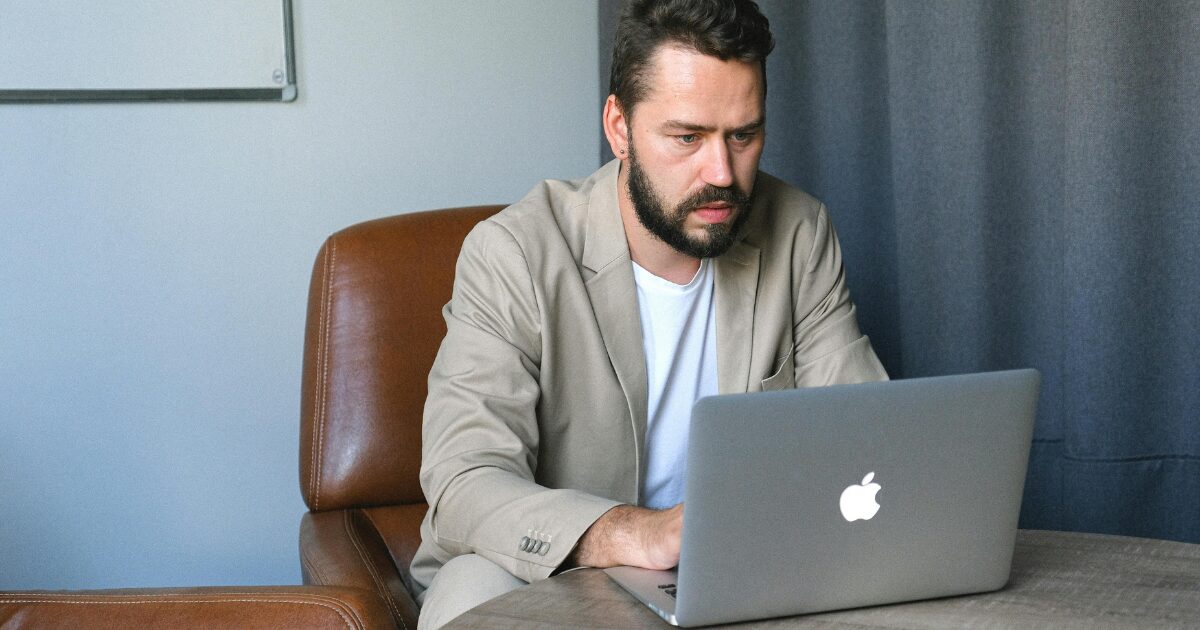 350 A Caucasian man wearing a beige blazer sitting while using his laptop.
