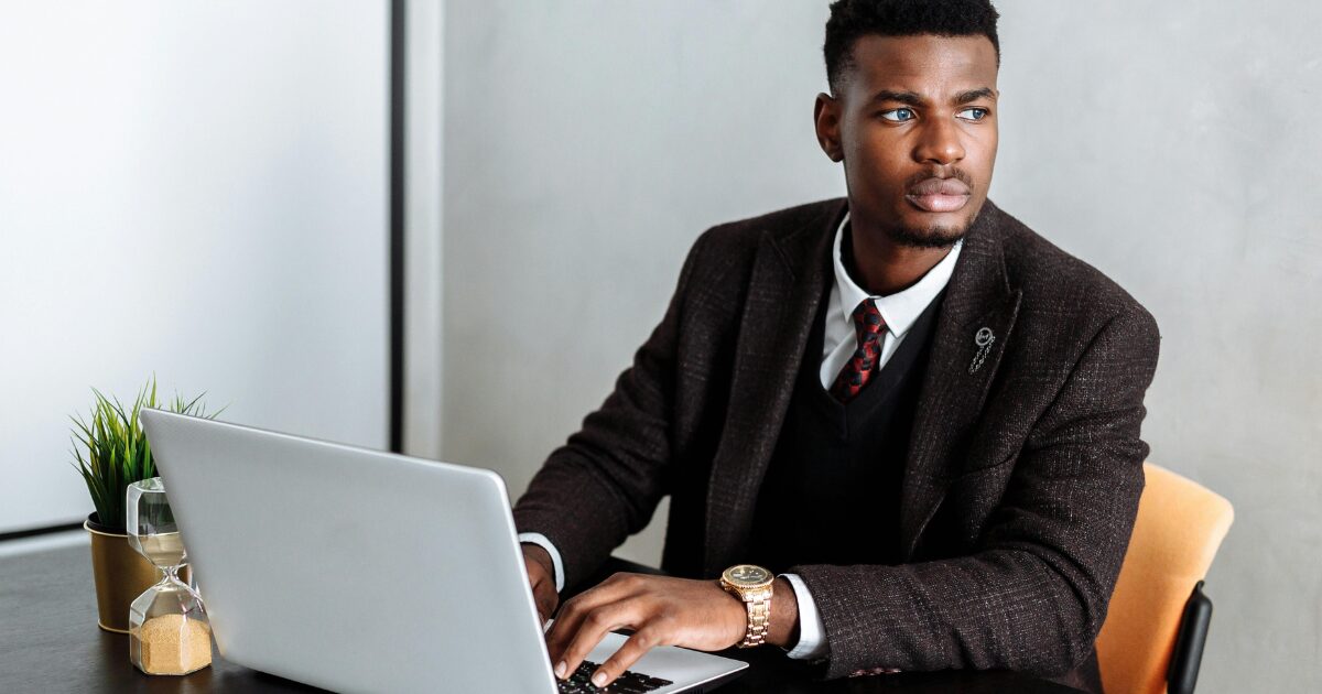 351 A Black man in a black business suit works on his laptop while glancing to the side.