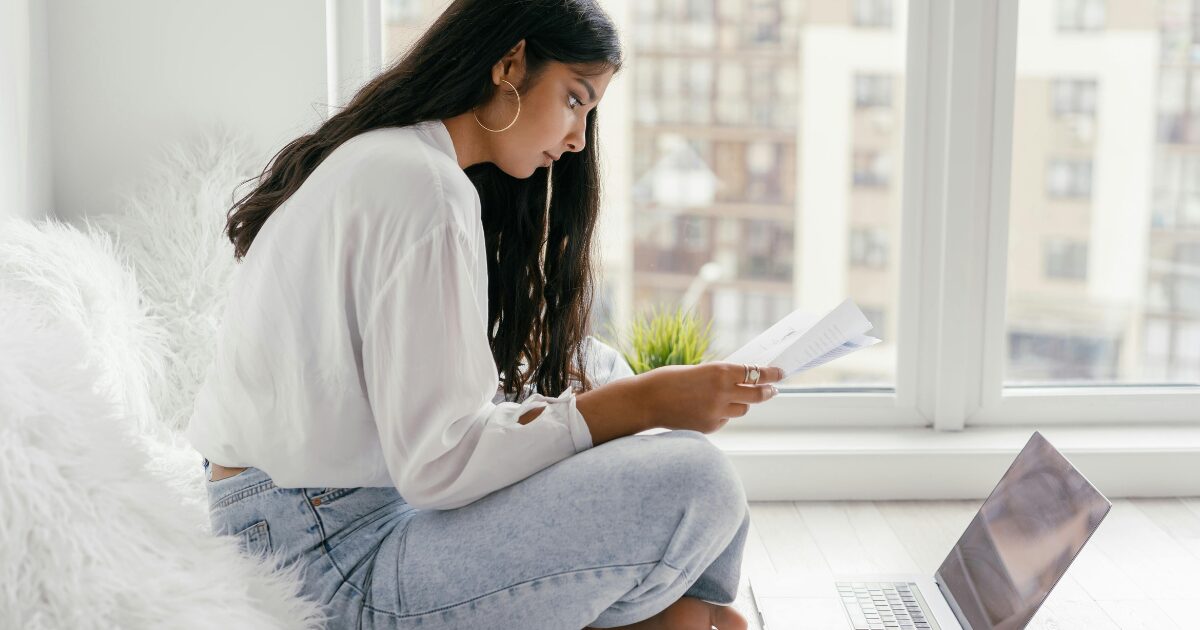352 An East Asian woman wearing a white blouse sits cross-legged on the floor while reading a document.