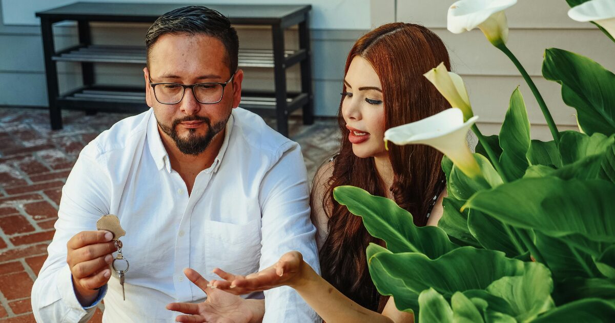 A Latino man wearing a white shirt holds a key while sitting beside a Latina woman.