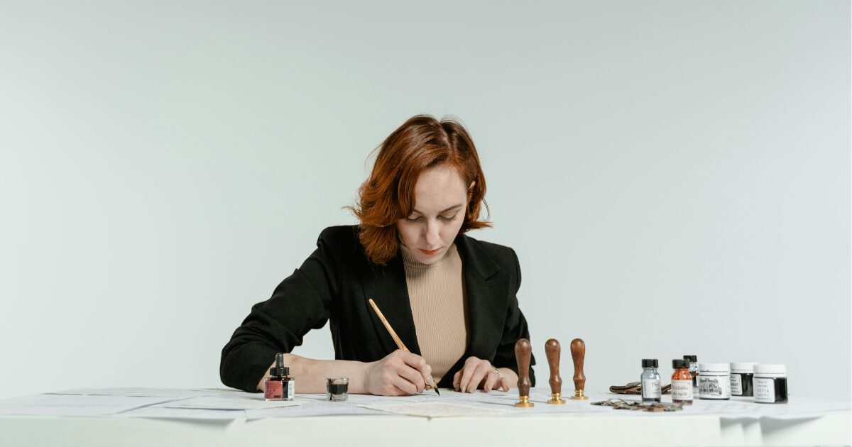 A Caucasian woman wearing a black blazer writes on a piece of paper.