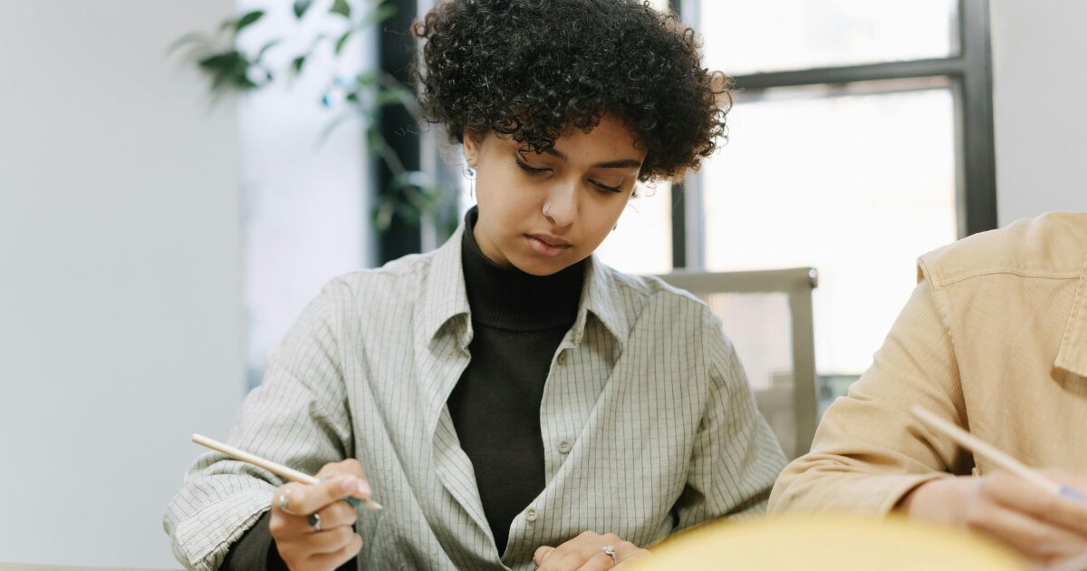 A Black woman wearing a light gray blazer holds a pen in her right hand.