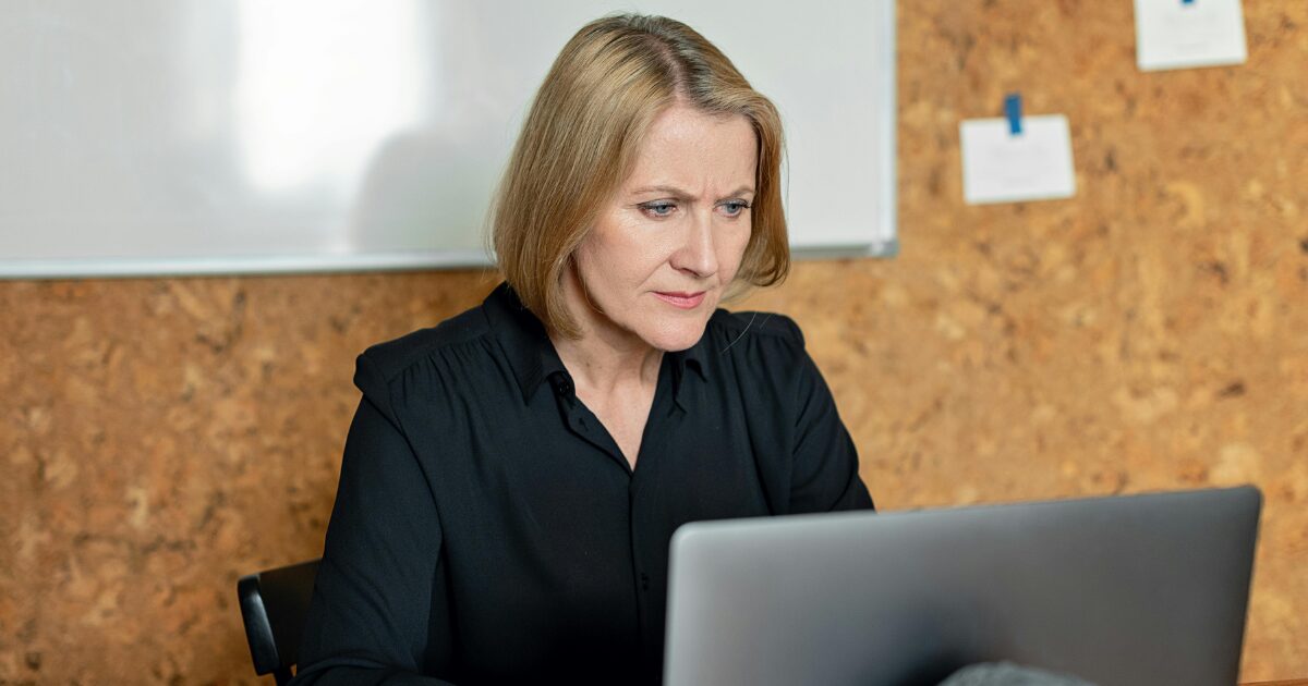 A Caucasian woman wearing a black long sleeve shirt is using a laptop.
