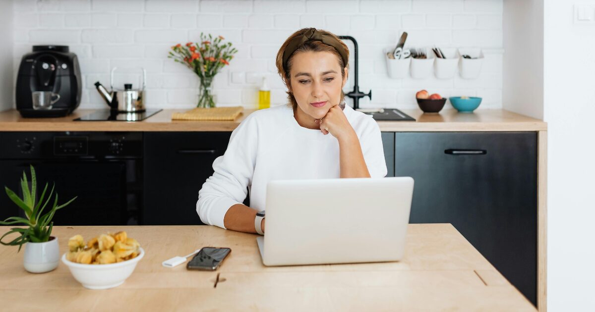 A Caucasian woman wearing a white sweater sits while using her laptop.