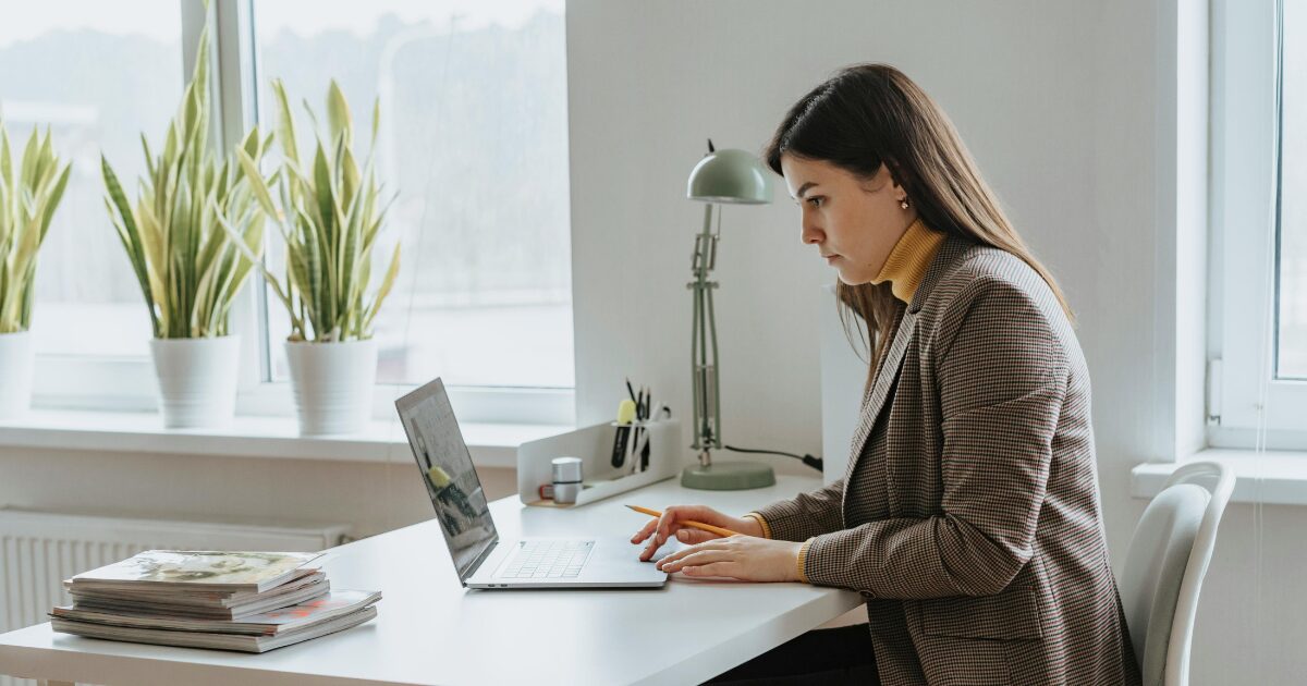 A Caucasian woman wearing a brown blazer uses her laptop while seated.
