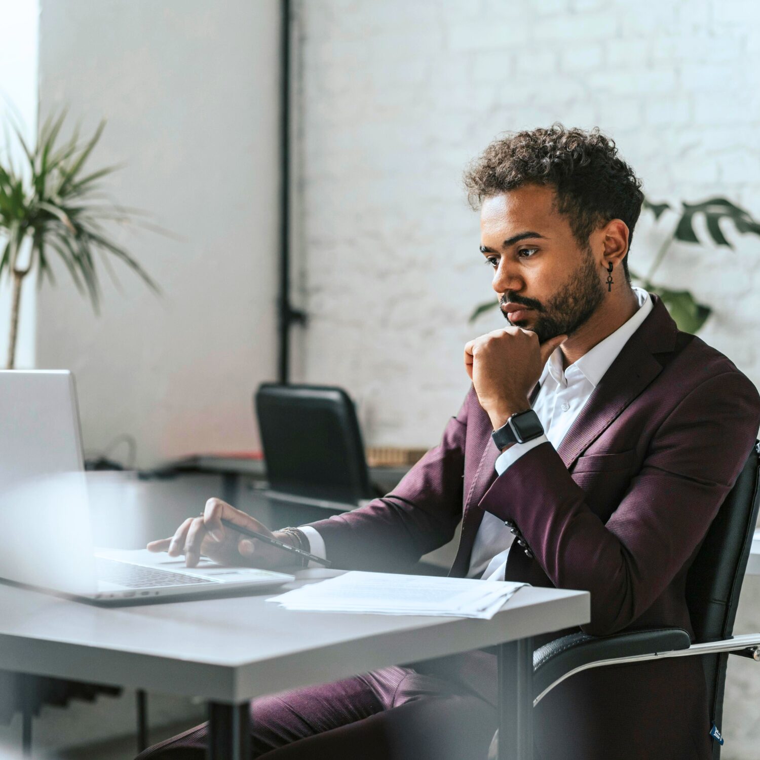 A South Asian man wearing a maroon business suit sitting while using his laptop.