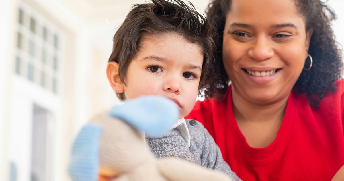 419 A Black woman wearing a red shirt smiles while beside a young Caucasian boy wearing a grey shirt.
