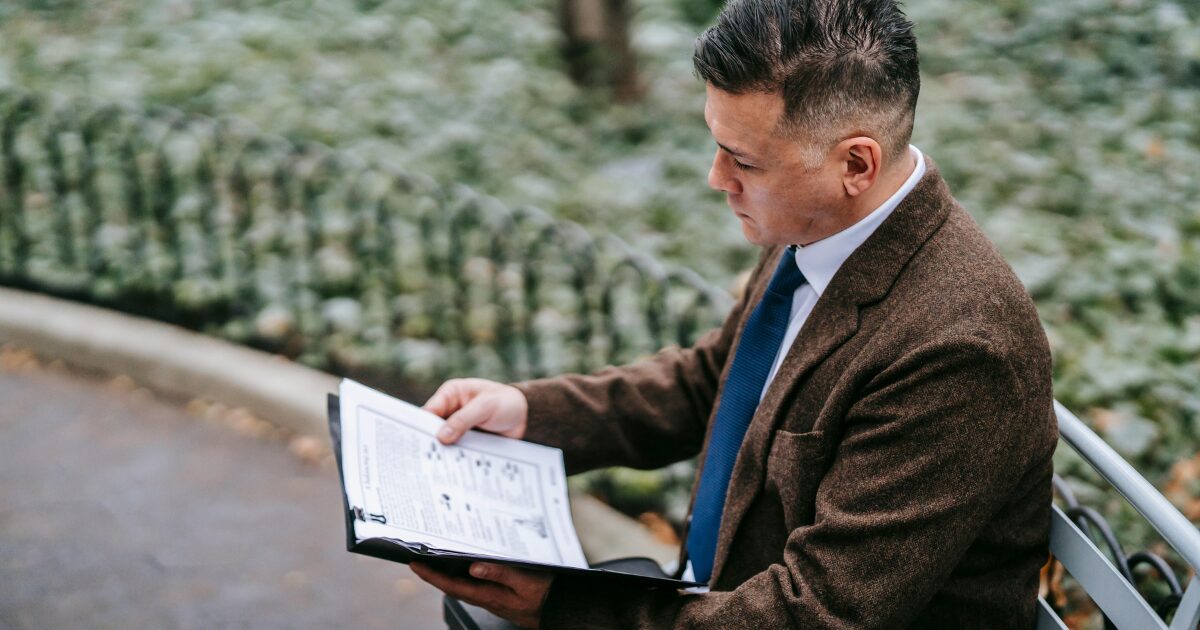 424 A Caucasian man wearing a brown business suit reads documents from a folder.