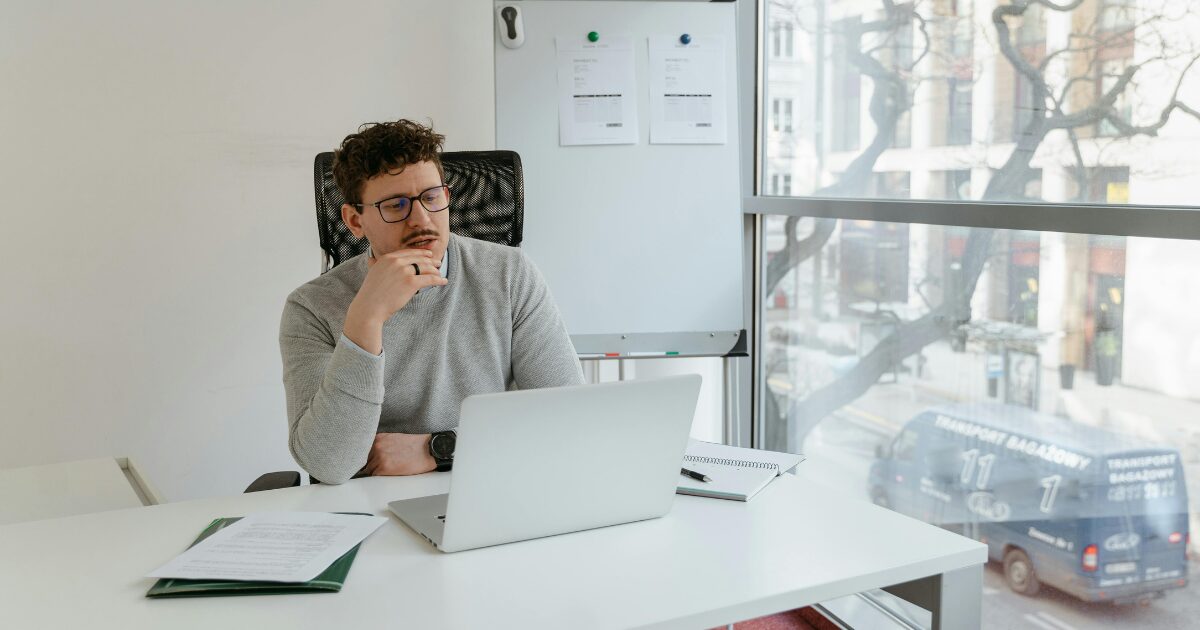 428 A Caucasian man wearing a light grey long-sleeve shirt sits in front of an open laptop.