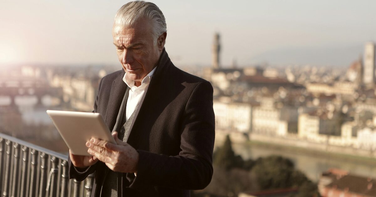 430 A Caucasian man wearing a black business coat using a tablet outdoors.