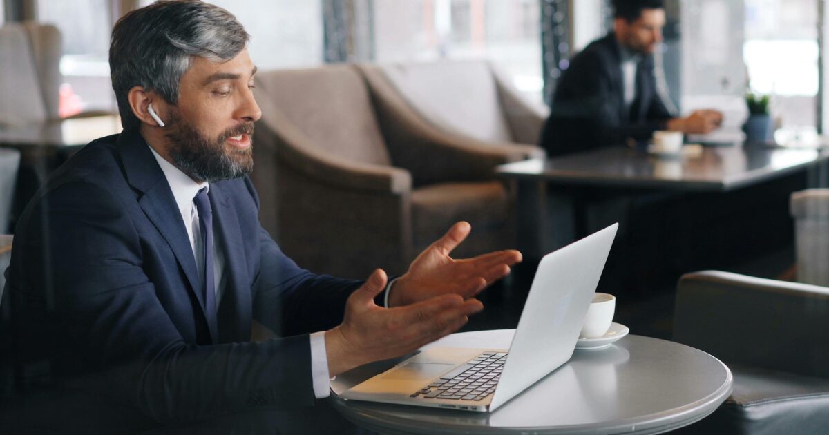 432 A Caucasian man wearing a black business suit talks during a video call on a laptop.
