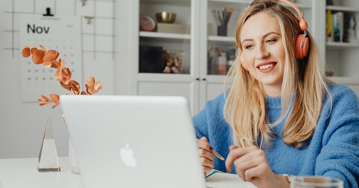 A Caucasian woman wearing a blue sweater smiles while using her laptop. 