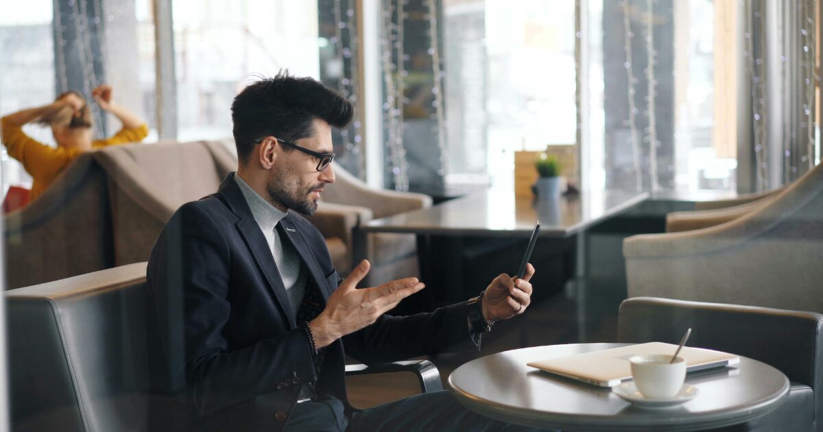 A Caucasian man wearing a black business suit on a video call using his phone.