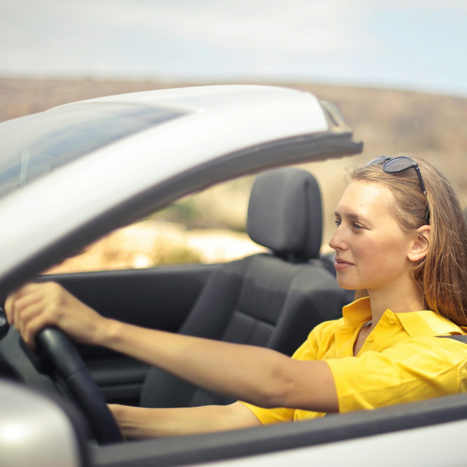A Caucasian woman wearing a yellow shirt driving a car.