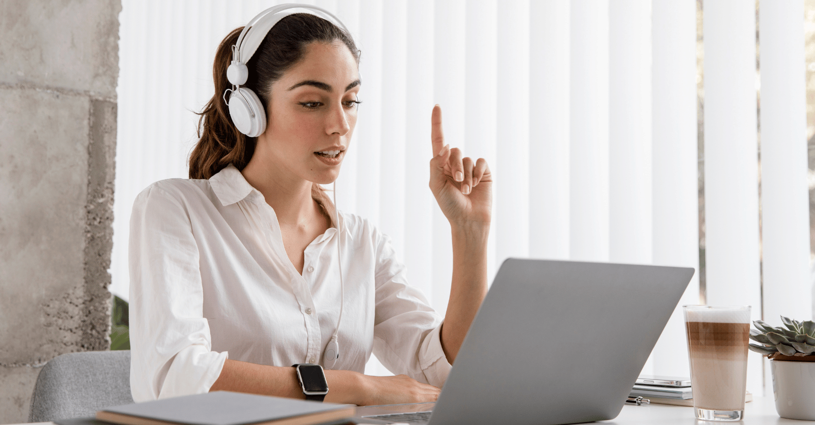 Woman wearing headphones raising a finger to ask a question during a video call on her laptop