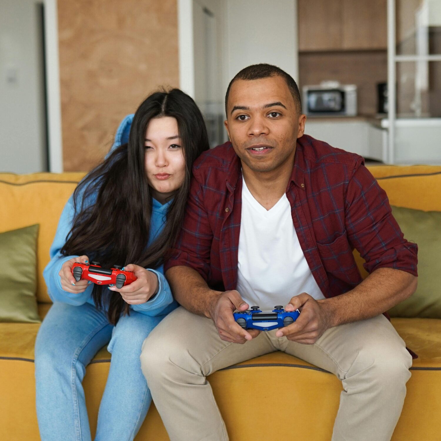 Young Asian woman and young Black man sitting side-by-side on a couch while they play video games.