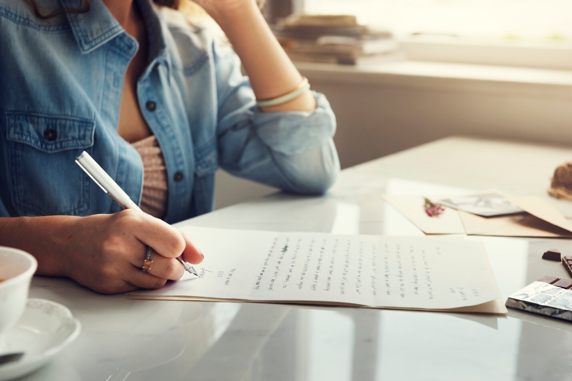 A woman witting at a table writing a letter with a pen