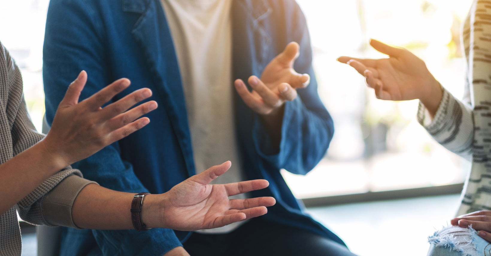 Three people gesture with their hands while having a conversation in a bright, professional setting.